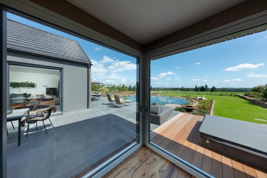 Blick durch die großzügigen Hebeschiebetüren aus Holz-Aluminium auf den Schwimmteich